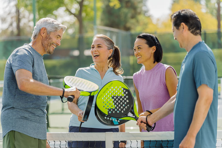 Grupo de amigos de edad madura sonriendo cómplices en el centro de la cacha de padel