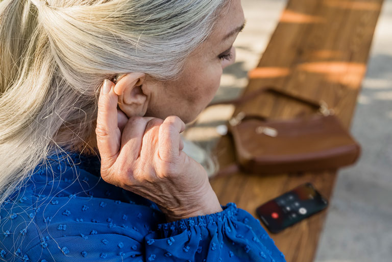 mujer madura de pelo largo canoso ajustando su audifono retroauricular derecho