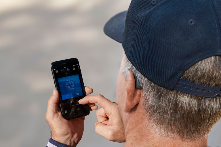 vista trasera de hombre adulto con audífono en su oreja izquierda , utilizando app movil beltone hear max