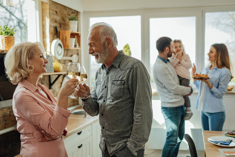 en primer plano, una pareja de adultos haciendo un brindis, en segundo plano un matrimonio joven junto a una niña en los brazos del hombre