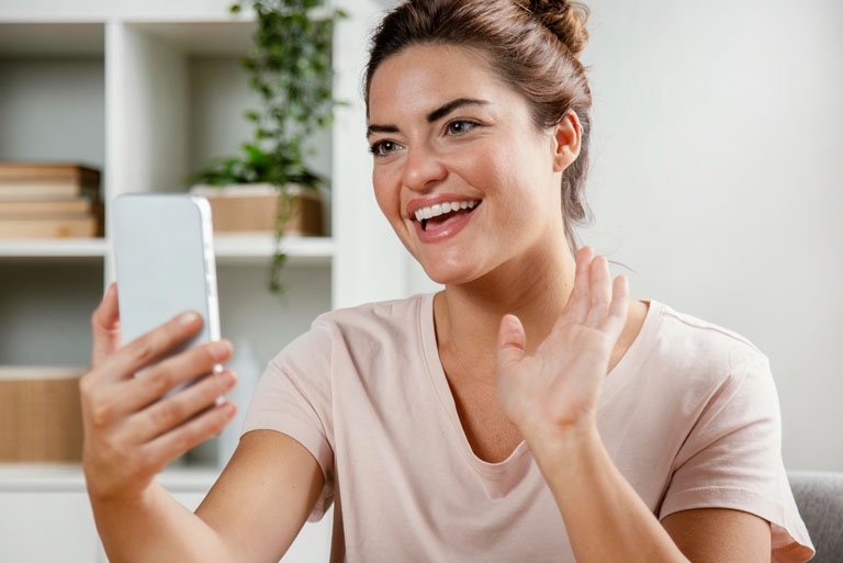 Mujer joven en video llamada con su teléfono movil sonriendo y saludando con la mano