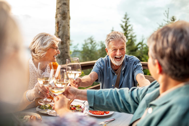 grupo de amigos de edad madura sentados en una mesa al aire libre brindando y sonriendo