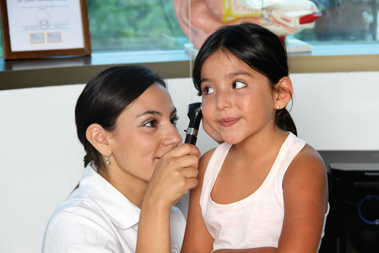 Tecnóloga médica de Auditron Chile revisando el oído de niña con otoscopio